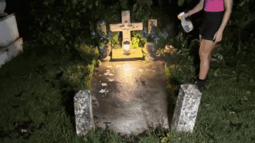 a woman stands in front of a grave with a cross and a candle lit up