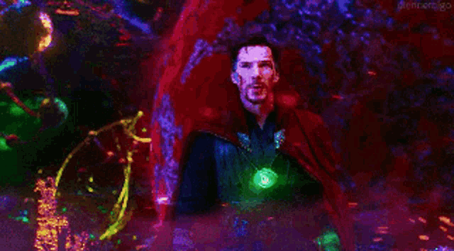 a man in a red cape is standing in a dark room holding a glowing pendant .