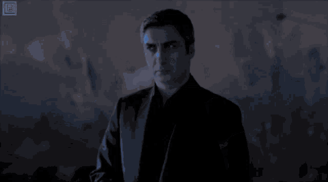 a man in a black suit stands in front of a blue sky with a yellow rectangle that says ' tb '