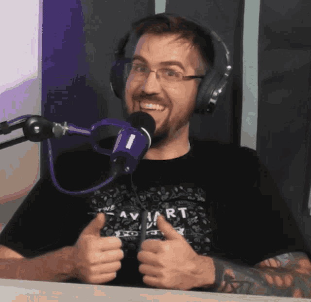 a man wearing headphones is giving a thumbs up in front of a blue microphone