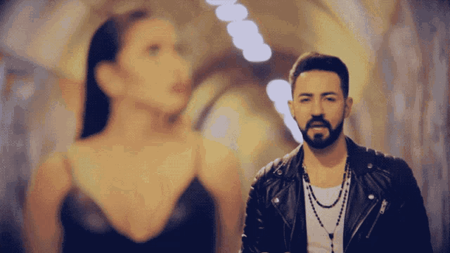 a man in a leather jacket stands next to a woman