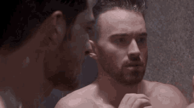 a shirtless man is looking at himself in the mirror .