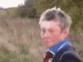 a young boy in a blue shirt and tie is standing in a field with his eyes closed .