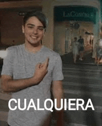 a young man in a gray shirt is giving the middle finger while standing in front of a store .