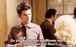 a man in a plaid shirt and tie is talking to a woman and says do you know that wildflower mural on the second floor