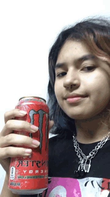 a girl is holding a red monster energy drink