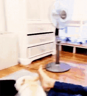 a person 's feet are laying on the floor in front of a fan
