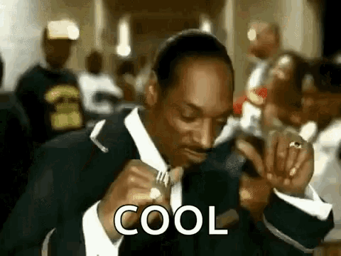 snoop dogg is wearing a suit and tie and smoking a cigarette in a room .
