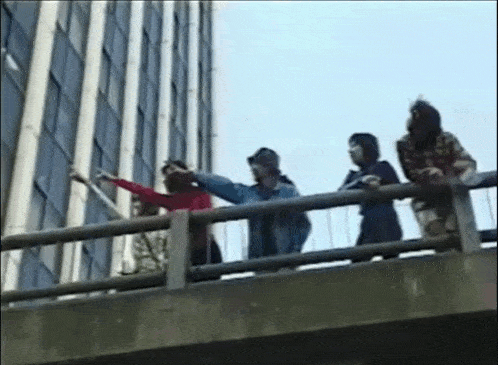a group of people are standing on the edge of a bridge looking out at a building .