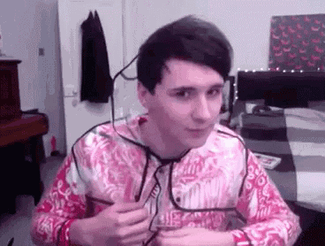 a young man wearing glasses and a pink shirt is sitting at a table in a room .