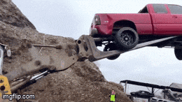 a red truck is being lifted by a crane on a pile of dirt .