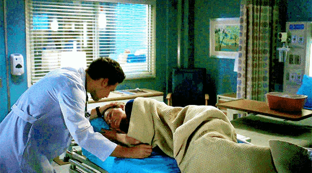 a doctor is putting a blanket on a patient 's head in a hospital bed .