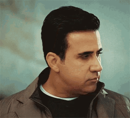 a man wearing a jacket and a black sweater is looking down .