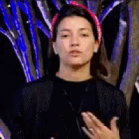a woman wearing a pink headband and a black jacket is making a gesture with her hands .