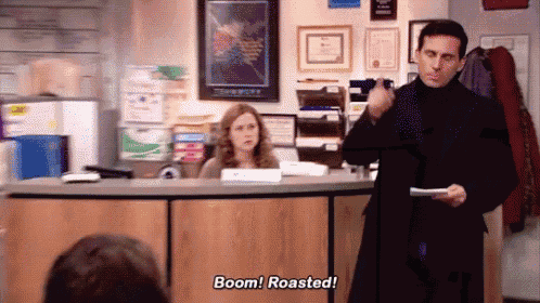 a man is standing in front of a desk holding a piece of paper and saying boom ! roasted !