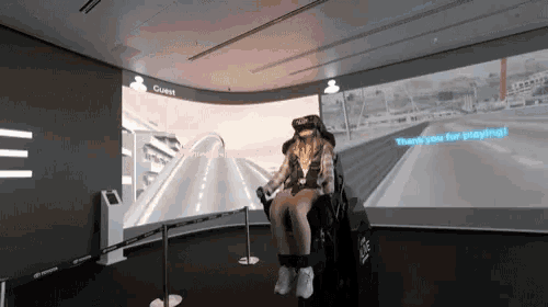 a woman wearing a virtual reality headset is sitting in front of a large screen that says guest