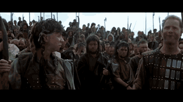 a group of men are standing in front of a crowd of people holding spears