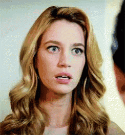 a woman with blonde hair and blue eyes is making a surprised face while looking at a man .