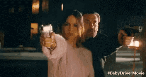 a man and a woman are pointing guns at each other in a movie scene .