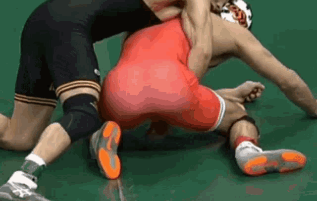 two men are wrestling on a green mat and one of them is wearing a red singlet .