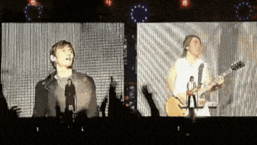 a man singing into a microphone while another man plays a guitar on stage