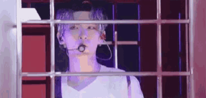 a man with purple hair and a microphone in his mouth is behind bars in a cage .