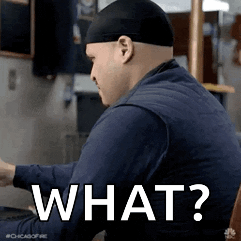 a man wearing a hat is sitting at a table with the words `` what '' written on the screen .