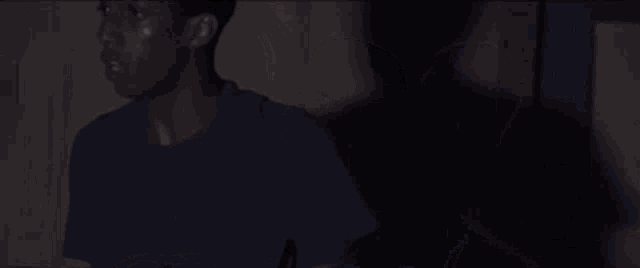 a man in a blue shirt is holding a hose in his hand in a dark room .