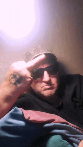 a man with sunglasses and a tattoo on his wrist giving the middle finger