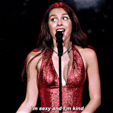 a woman in a red dress is singing into a microphone and saying i 'm sexy and i 'm kind