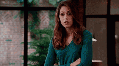 a woman in a blue sweater is standing with her arms crossed and looking at the camera .