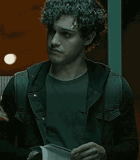 a young man with curly hair and a bandage on his forehead is holding a piece of paper in his hand .