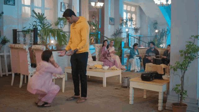 a man in a yellow hoodie stands next to a woman in a pink dress in a living room .