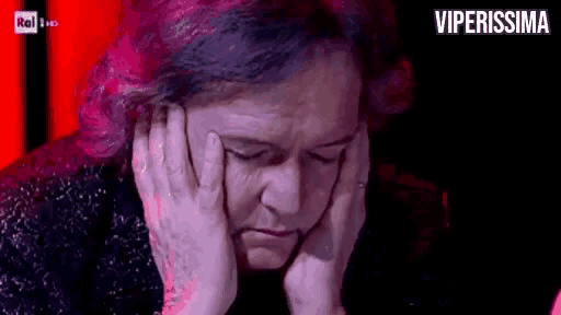 a woman with pink hair is covering her face with her hands and looking down .