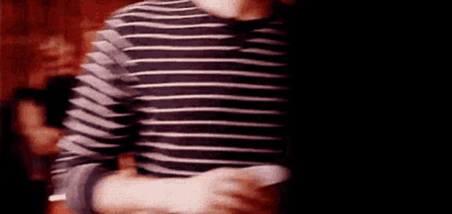 a man in a striped shirt is holding a remote control in his hand .