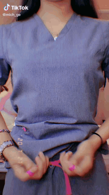 a tiktok video of a woman in scrubs with pink nail polish