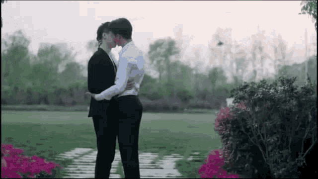 two men are kissing in a park with trees in the background .