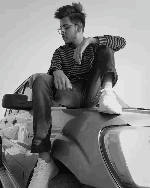a black and white photo of a young man sitting on a car