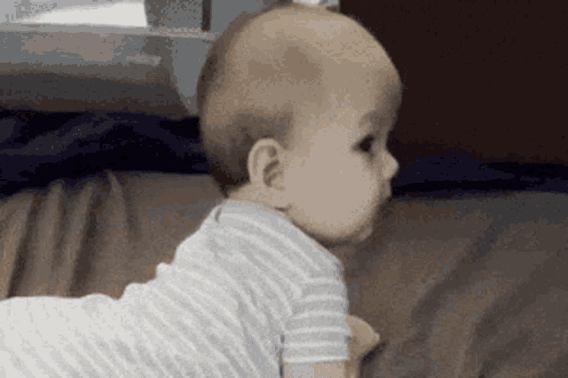 a baby is crawling on a bed and looking at something .