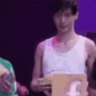 a man in a white tank top is standing in front of a purple background holding a box .