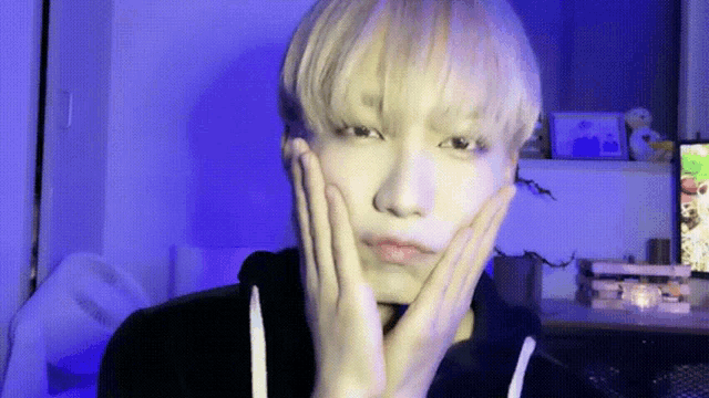 a young man with blonde hair is making a funny face with his hands on his face