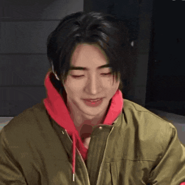 a young man wearing a green jacket and a red hoodie smiles