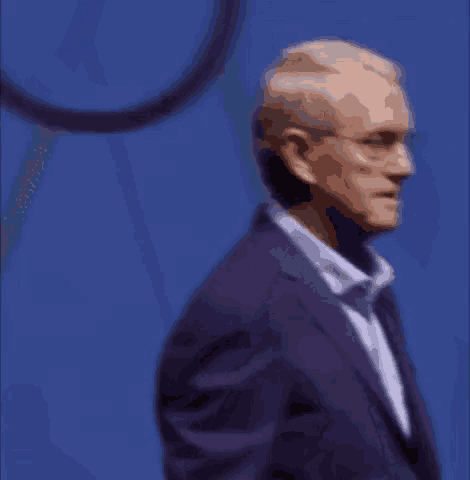 a man wearing a purple suit and glasses is standing in front of a blue background .