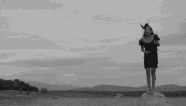 a woman in a black dress is standing on a rock in the middle of a desert .