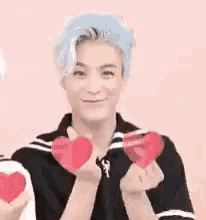 a young man with blue hair is holding a red heart in his hands .