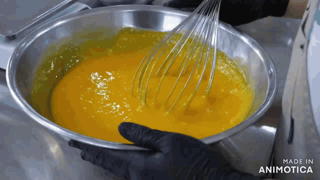a person is whisking a yellow liquid in a metal bowl which is made in animotica