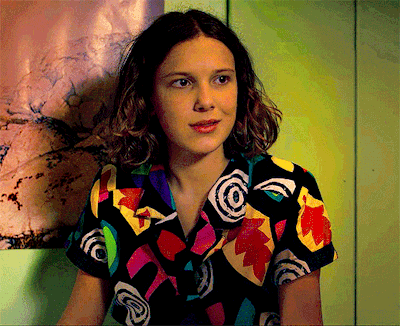 a girl wearing a colorful shirt is sitting in front of a green wall .