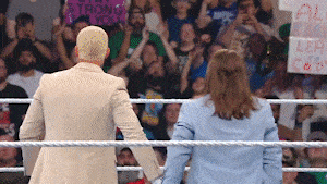 a man and a woman are standing in a wrestling ring with a crowd behind them