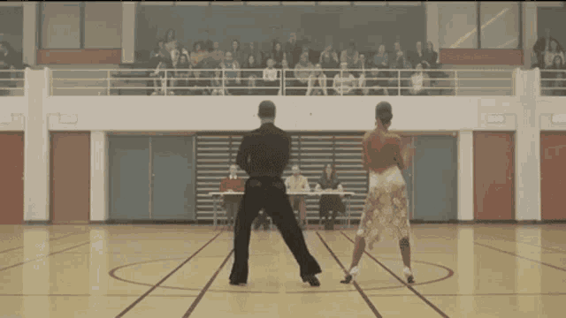 a man and a woman are dancing on a court with a crowd watching