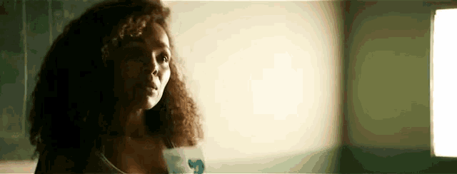 a woman with curly hair is standing in a room with a window .
